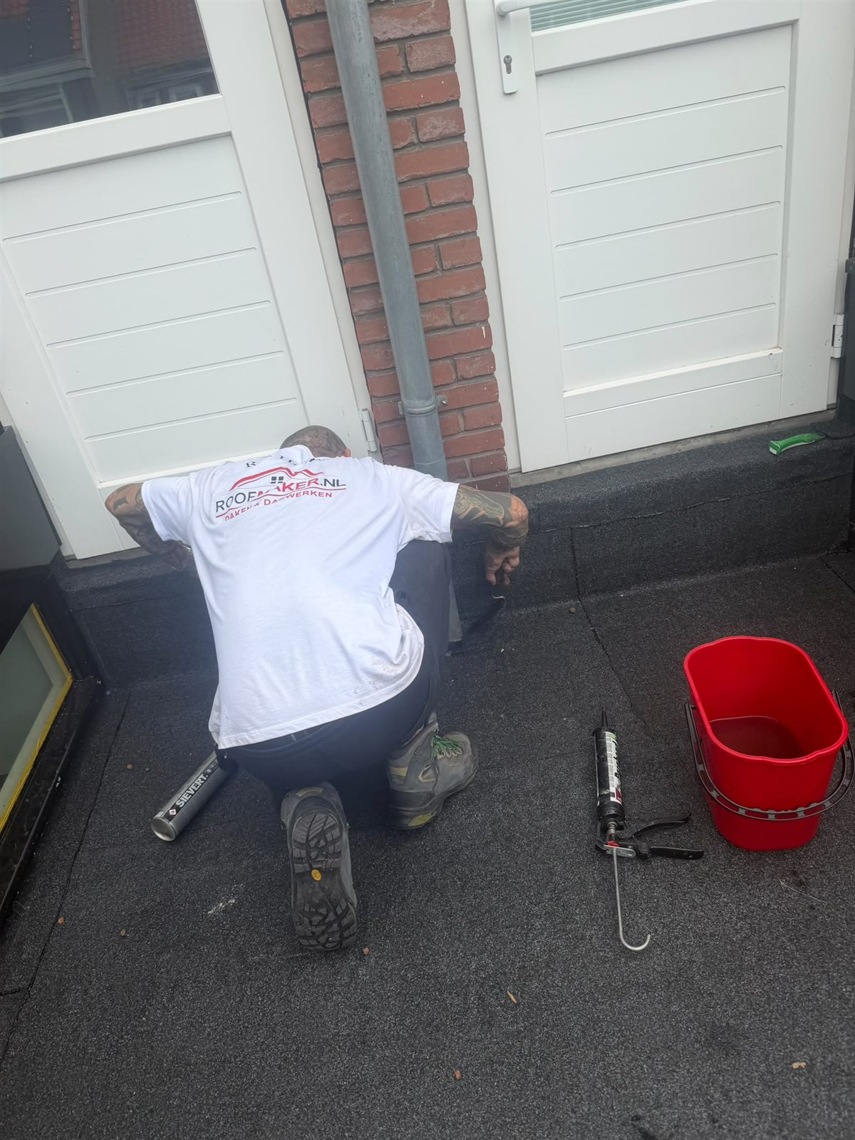 Dakdekker werkt aan bitumen dakbedekking bij een binnenplaats